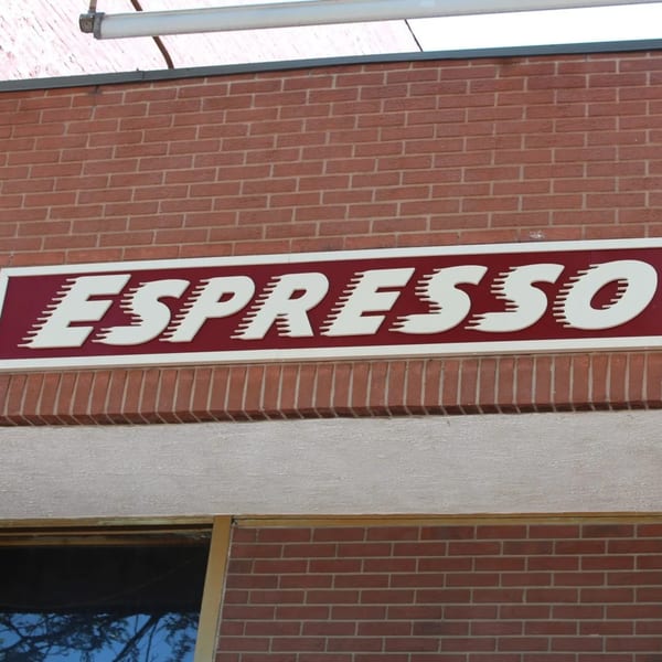 The red and white "Espresso" sign on a brick building, with a window below.