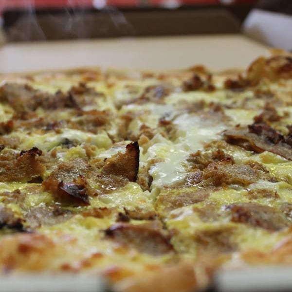 Steaming hot Espresso Pizza with melted cheese and meat toppings, sliced in a cardboard box.