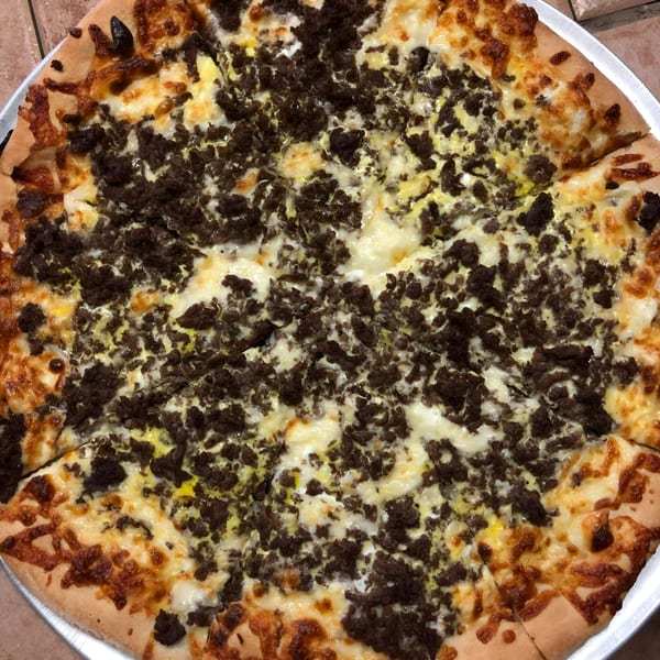 A whole Espresso Pizza with white cheese and generous crumbled sausage toppings, sliced and ready to eat.