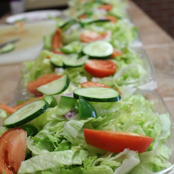 Multiple fresh garden salads with lettuce, tomatoes, cucumbers, and peppers in clear containers.