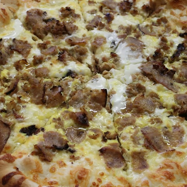 Close-up of a sliced Espresso Pizza breakfast pizza with sausage, egg, and cheese.