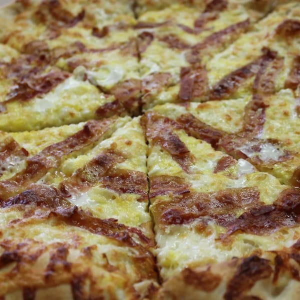 A close-up of a freshly baked Espresso Pizza, cut into slices, with melted cheese and crispy bacon.