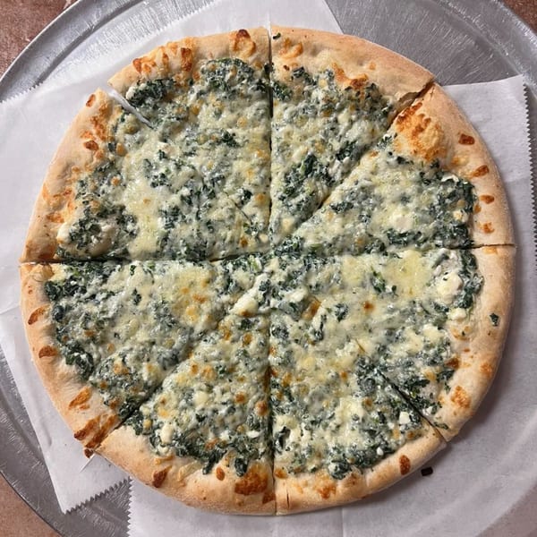 A whole spinach and feta pizza, cut into eight slices, on a metal pizza pan.