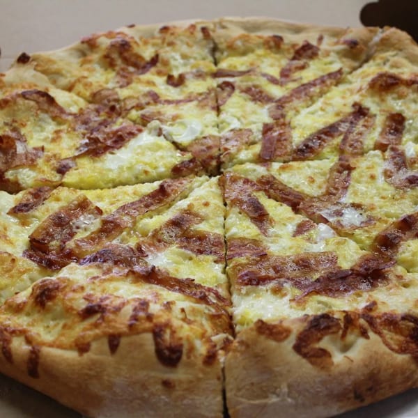 Close-up of a freshly baked Espresso Pizza with a white sauce base and bacon strips.